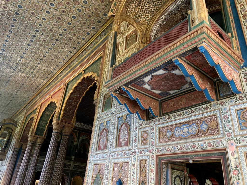 The painted hall: scalloped arches, teak columns, a frescoed ceiling